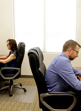 Two individuals working independently at separate desks in a neutral-toned office.