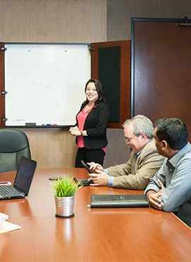 Woman presenting at a whiteboard while three colleagues listen at a conference table.
