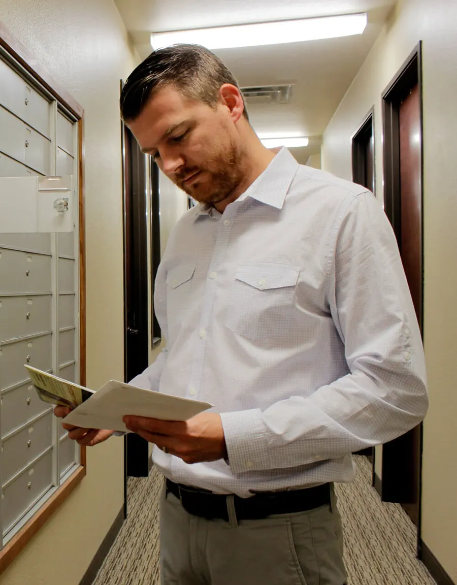 Person reading mail beside a wall-mounted mailbox unit in a well-lit building.